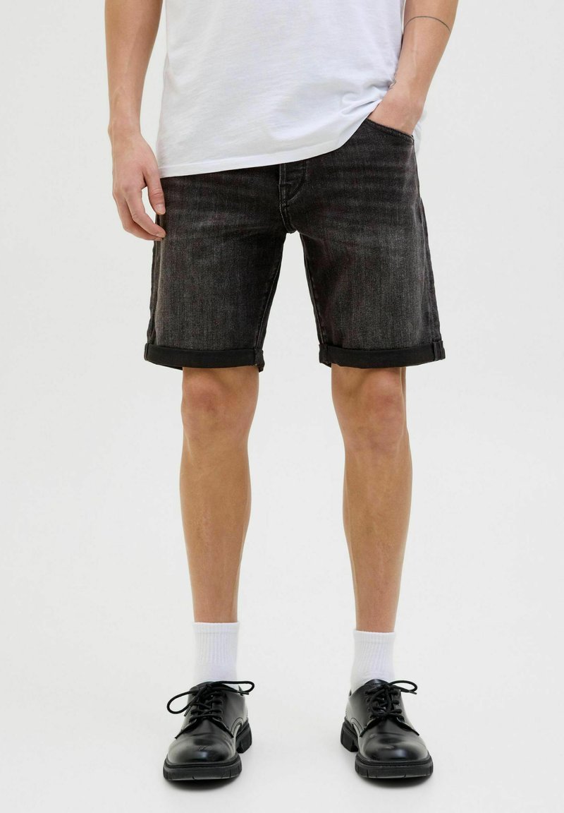 Șorturi din denim negre cu manșete răsucite, având un design clasic cu cinci buzunare. Asortate cu șosete albe până la gleznă și pantofi negri cu șireturi.