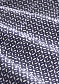 Tissu bleu marine avec un motif géométrique répétitif d'ovales blancs formant des formes circulaires avec de petits points bleus aux intersections, présenté avec des plis doux.