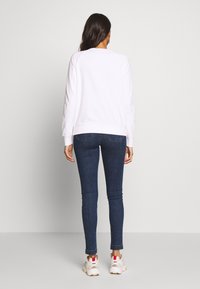 Felpa bianca con scollo rotondo, vestibilità ampia e orlo a costine, abbinata a jeans skinny blu scuro e sneaker bianche.