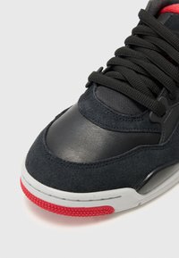 Baskets en daim noir et cuir synthétique avec semelle grise et accents rouges. Dotées de lacets noirs épais et d'un design à bout arrondi.