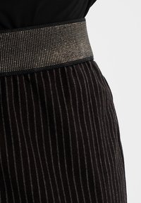 Černá pruhovaná látka s texturovaným sametovým povrchem a širokým pasaem s metalickým akcentem. Obsahuje vertikální jemné pruhy pro detail.