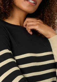 Gestreifter Pullover in Schwarz und Creme mit rundem Halsausschnitt und langen Ärmeln, aus weichem Strickstoff und sichtbaren Nahtdetails.