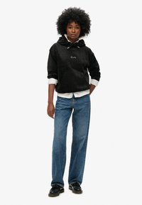 Felpa nera con cappuccio, tasca frontale e ricamo "Signature". Abbinata a jeans blu a gamba dritta e scarpe nere.