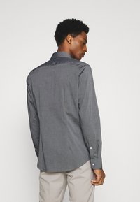 Grijze shirt met lange mouwen, voorzien van een gestructureerd patroon, een subtiele glans op de kraag en schouders, en knopenmanchetten. Draag het met lichte broek.