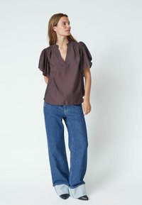 Top marrone a maniche corte con scollatura a V e dettaglio sulle spalle arricciato, abbinato a jeans denim a gamba larga con orlo a contrasto.
