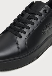 Baskets en cuir noir Calvin Klein avec lacets noirs, logo embossé sur le côté, et semelle épaisse en caoutchouc texturé.