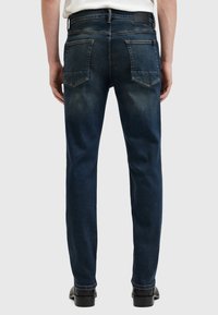 Jeans de denim azul oscuro con corte ajustado, que presentan dos bolsillos traseros, un ligero desvanecimiento y una etiqueta de cuero en la cintura.