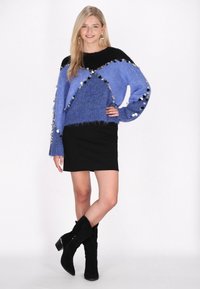 Maglione lavorato a maglia blu e nero con paillettes circolari lungo le maniche, abbinato a una mini gonna nera e stivali neri alti fino al ginocchio.