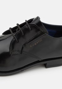 Chaussure de ville noire en cuir poli à lacets avec talon bas et nom de la marque Bugatti sur le côté.