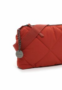 Bolso rojo acolchado con una superficie texturizada, que cuenta con una correa de cadena y una etiqueta con el logo. Incluye un cierre de cremallera y un diseño de color sólido.