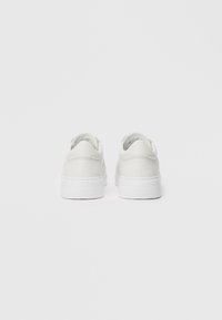 White sneakers with a smooth leather upper and textured accents, featuring a thick, white rubber sole and minimalistic design.