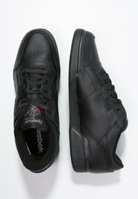Černé sportovní boty s hladkým koženým svrškem, se vzory perforací, kulatými tkaničkami, polstrovaným límcem a texturovanou gumovou podešví.