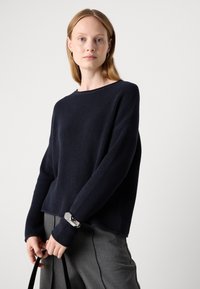 Maglione a costine blu navy con vestibilità rilassata, scollo ampio e maniche lunghe. Presenta un tessuto testurizzato e un orlo leggermente accorciato.