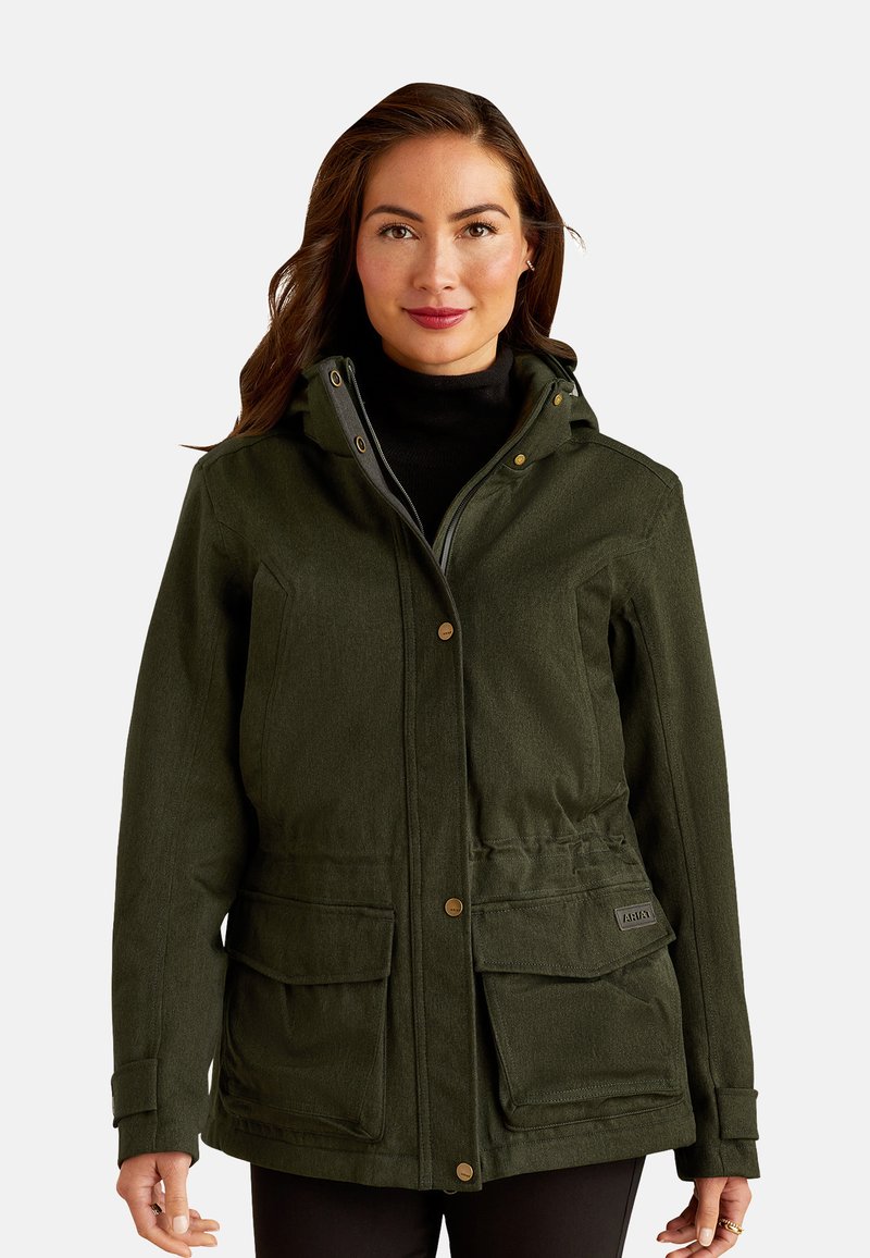 Groene jas met een gestructureerde afwerking, voorkantzakken, knoopsluiting, een hoge kraag en een capuchon. Draagt over een zwarte top.