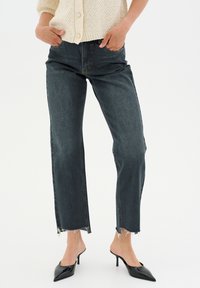 Mörk tvättade jeans med rak passform, råa fållar och en klassisk fem-fickors design, tillsammans med svarta klacktofflor.