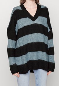 Oversized sweater with a V-neck, featuring wide black and light blue horizontal stripes. Made of textured knit fabric with ribbed hems.