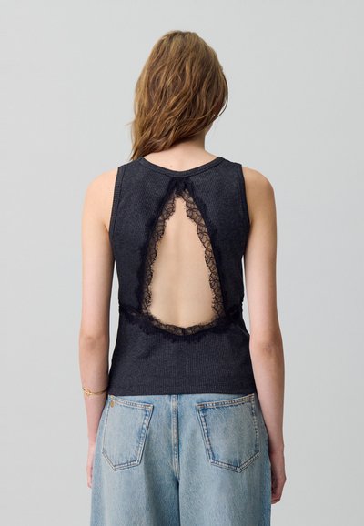 Top sin mangas negro con relieve que presenta un gran corte con encaje en la parte posterior; combinado con pantalones cortos de mezclilla de lavado claro.