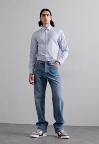 Cămașă butonată cu dungi albastre deschise, asociată cu blugi largi albaștri și adidași gri. Design simplu, croială standard, textură netedă.