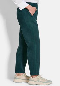 Groene suede broek met zijzakken, rechte snit en een zachte textuur. Draag ze met crèmekleurige en teal sneakers met een robuuste zool.