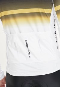 Weißes Sportshirt mit einem gradienten Muster aus schwarzen und gelben Horizontalstreifen. Verfügt über eine Rückentasche und die "ENDURANCE"-Markierung an der Seite.