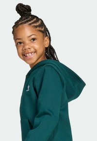 Sweatshirt à capuche teal avec une poche avant et un logo blanc. Le tissu semble doux avec une texture lisse. L'enfant a les cheveux en tresses.