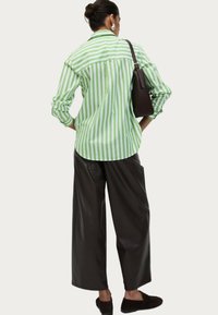 Groen en wit gestreepte button-up shirt met lange mouwen, gecombineerd met brede donkere broek. Een bruine handtas en zwarte instappers maken de look compleet.