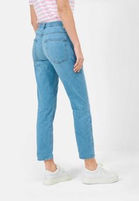 Jeans de mezclilla azul claro con corte recto, cintura alta y piernas ajustadas. Presentan dos bolsillos traseros y un dobladillo arqueado, combinados con zapatillas blancas.