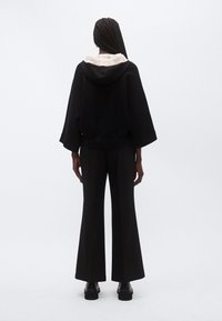 Sudadera con capucha negra con forro beige en la capucha, mangas anchas, combinada con pantalones acampanados negros de cintura alta. Textura suave, diseño minimalista.