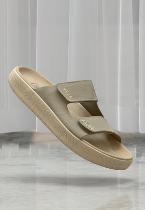 Sandales slip-on beige clair avec un dessus en daim texturé, des straps Velcro ajustables et une semelle en caoutchouc beige épaisse et à motifs.