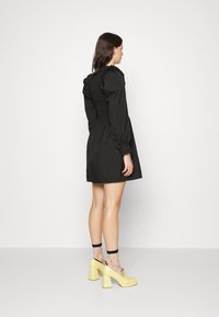 Rochie neagră cu mâneci puff, cu spate elastic, de lungime deasupra genunchiului, asortată cu pantofi cu platformă galbeni și șosete cu buline.