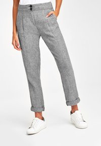 Lichtgrijze linnen broek met een gestructureerde afwerking, voorzien van een knoopsluiting in de taille, zijzakken en opgerolde boorden, gecombineerd met witte sneakers.