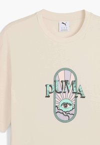 Cremefarvet bomulds-T-shirt med et grafisk print, der viser et stiliseret øje, solstråler og ordet "PUMA" i fede sorte bogstaver.