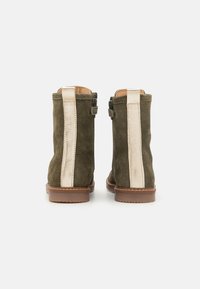 Stivaletti alla caviglia in suede verde con dettagli in pelle crema e una suola in gomma marrone. Presentano una fibbia laterale e una texture liscia.