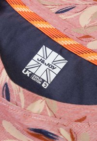 Bloemenpatroon stof in roze en beige tinten met marineblauwe voering. Toont een witte logo-tag met "J&JOY" en een ontwerp van de Britse vlag.