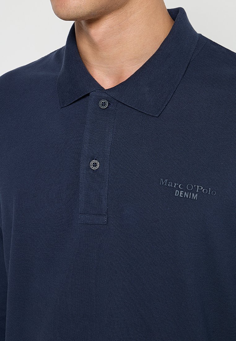Dunkelblauses Polohemd aus strukturiertem Stoff, mit Kragen, zwei Knöpfen und dezentem Branding "Marc O'Polo DENIM" auf der Brust bedruckt.