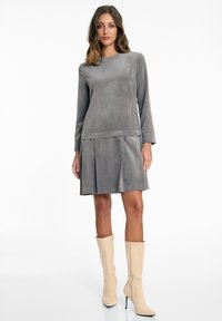 Graues Cordkleid mit langen Ärmeln, plissiertem Rock und rundem Ausschnitt, kombiniert mit beigen Stiefeln mit hohem Absatz bis zum Knie. Glatte Textur.