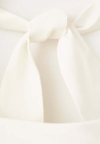Gros plan d'un nœud en tissu blanc noué sur un fond de matériau doux à texture lisse.