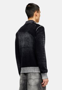 Pull en tricot noir avec un design en dégradé texturé, ourlet et poignets côtelés, col avec un col et des détails en blanc le long des épaules.