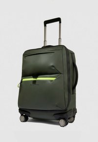 Groene handbagagekoffer met een gladde, duurzame buitenkant, voorzien van een voorvak met een heldergele rits, een intrekbare handgreep en vier wielen.