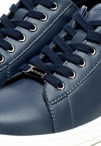 Sneakers in pelle blu con lacci in tessuto, occhielli argentati e un accento di logo metallico. Presentano un design testurizzato e una suola in gomma bianca.