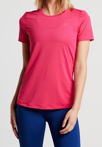 Camiseta deportiva de manga corta en poliéster rosa brillante, con escote redondo y un logo sutil. Textura suave y diseño ajustado.