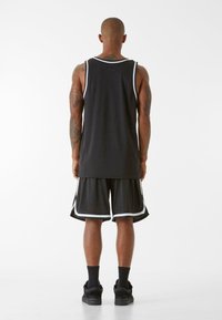Melnā bezpiedurkņu basketbola krekls ar baltu apdari, apvienots ar melniem šortiem, kuriem ir baltas akcenti. Stingrs audums, brīvs piegriezums.