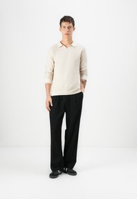 Lys beige strikket genser med V-hals, lange ermer, kombinert med sorte vide bukser og sorte sneakers. Enkel og uprydet design.