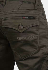 Dunkelolivgrüne Cargo-Hosen mit detaillierten Nähten, einem Knopfverschluss und einem sichtbaren Logoetikett an der Rückentasche.
