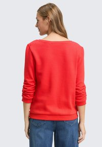 Rode sweatshirt met een brede hals, lange mouwen en geribbelde boorden. Zachte textuur, gecombineerd met blauwe jeans, gezien vanaf de achterkant.