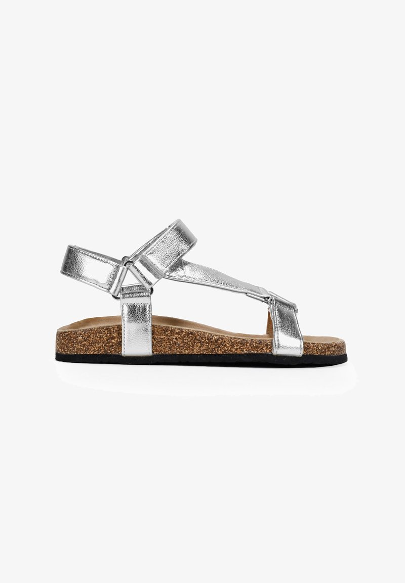 Silberne metallische Sandalen mit Korkfußbett, ausgestattet mit zwei verstellbaren Riemen und einer flachen Gummisohle in Schwarz. Minimalistisches Design, offene Zehen.