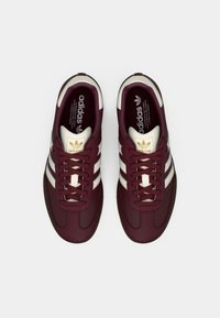 Par tid maroon Adidas sneakers med hvide striber og guld logo accenter, vist ovenfra på en hvid baggrund.