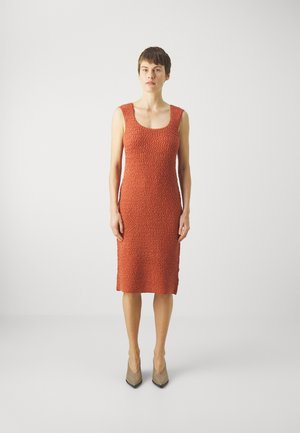 Rust-colored, sleeveless dress with a textured pattern, knee length, and a scoop neckline. Worn with beige pointed heels.