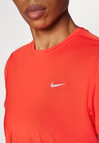 Piros Nike sport póló, sima és könnyű anyagból készült. Kerek nyakkivágással és apró szürke logóval rendelkezik a mellkason.