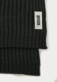 Sciarpa grigia scura lavorata a maglia con una texture a coste e un'etichetta bianca con il nome del marchio "DRYKORN" cucita su un bordo.